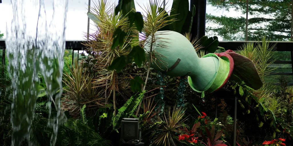 A green stuffed animal sitting on top of a lush green plant